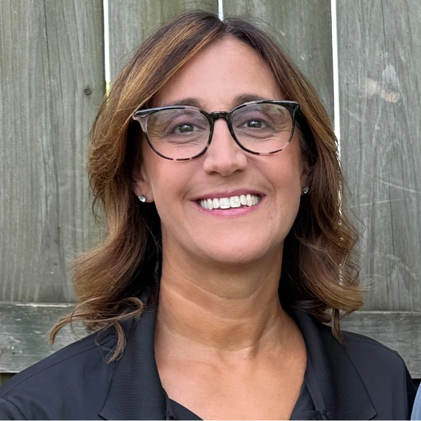 a woman wearing glasses is smiling in front of a wooden fence. - Prestige Pools - Prestige Pools a woman wearing glasses is smiling in front of a wooden fence.