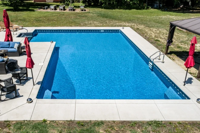 an aerial view of a swimming pool in a backyard. - Prestige Pools A 20x43x28 vinyl liner pool in a True L shape with plastic steps and benches