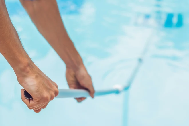 a person holding a broom in a swimming pool. - Prestige Pools A close up of a person cleaning a pool