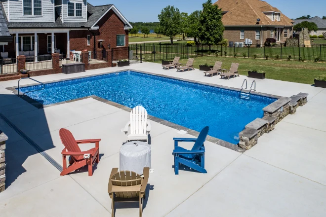 A backyard with a swimming pool and lawn chairs. - Prestige Pools A True L shape vinyl liner pool with vinyl steps & a waterfall