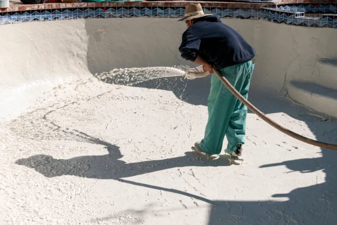 A man using a hose to clean a pool. - Prestige Pools A concrete pool installer sprays plaster on a concrete pool shell