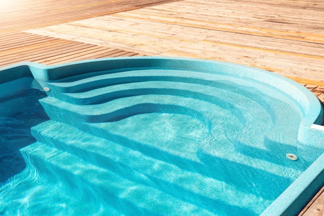 A swimming pool on a wooden deck. - Prestige Pools fiberglass plastic swimming pool entrance step with clean fresh refreshing blue water