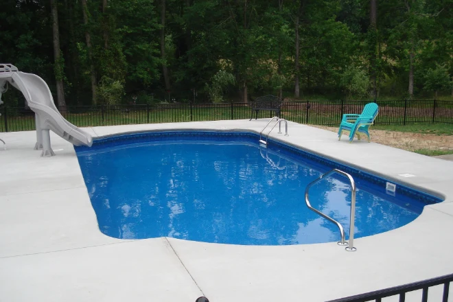 A swimming pool with a slide and chairs.