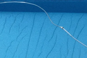 A pool vacuum hose rests on the textured blue floor of an empty or partially filled swimming pool. wrinkles in pool liner - floating pool liner causes